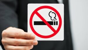 禁煙マークのサインを手に持つ人。赤い円と斜線でタバコが禁止されていることを示す標識。